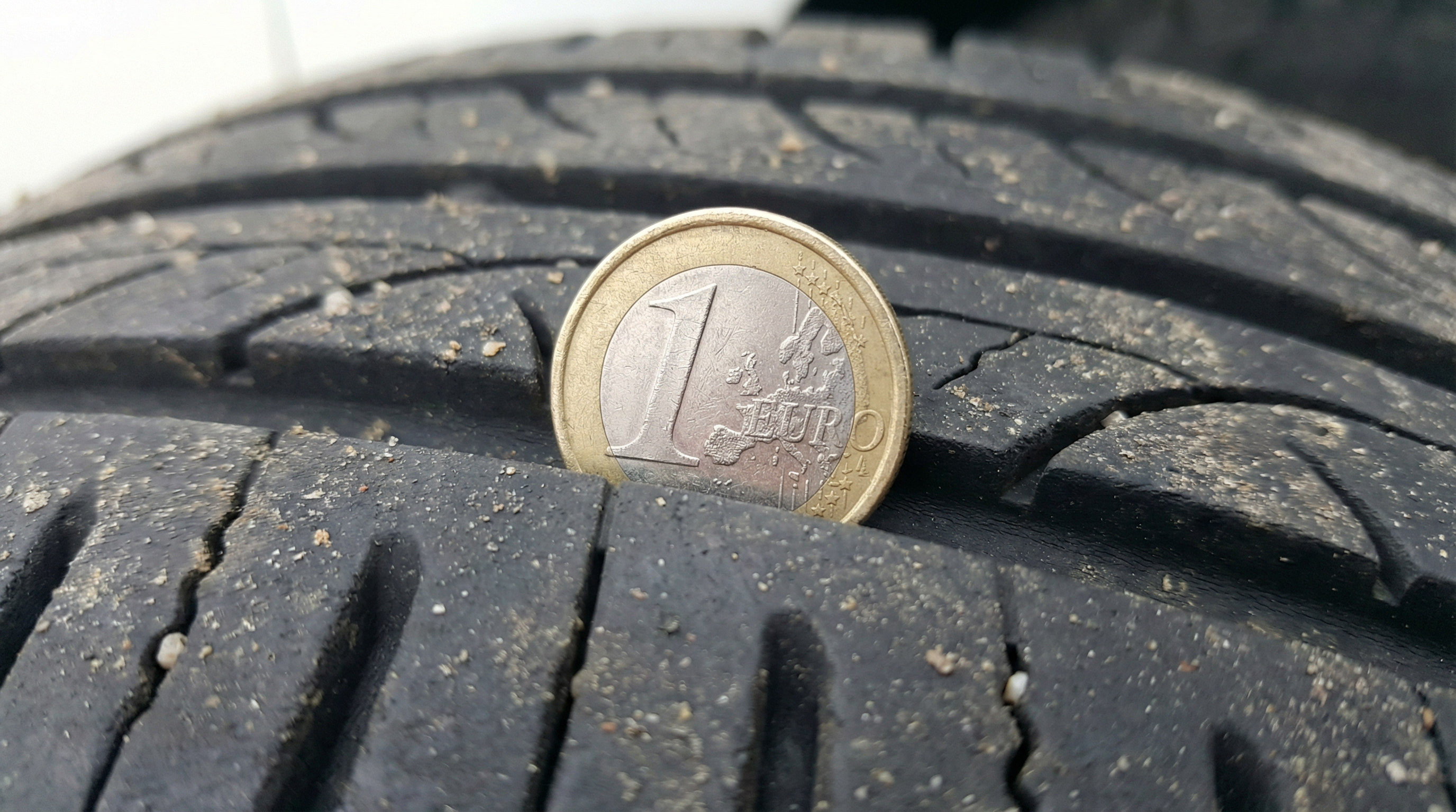 Dica: Close-up macro e super nítido de uma moeda de 1 euro inserida nas ranhuras de um pneu em bom estado (com a borda dourada escondida)